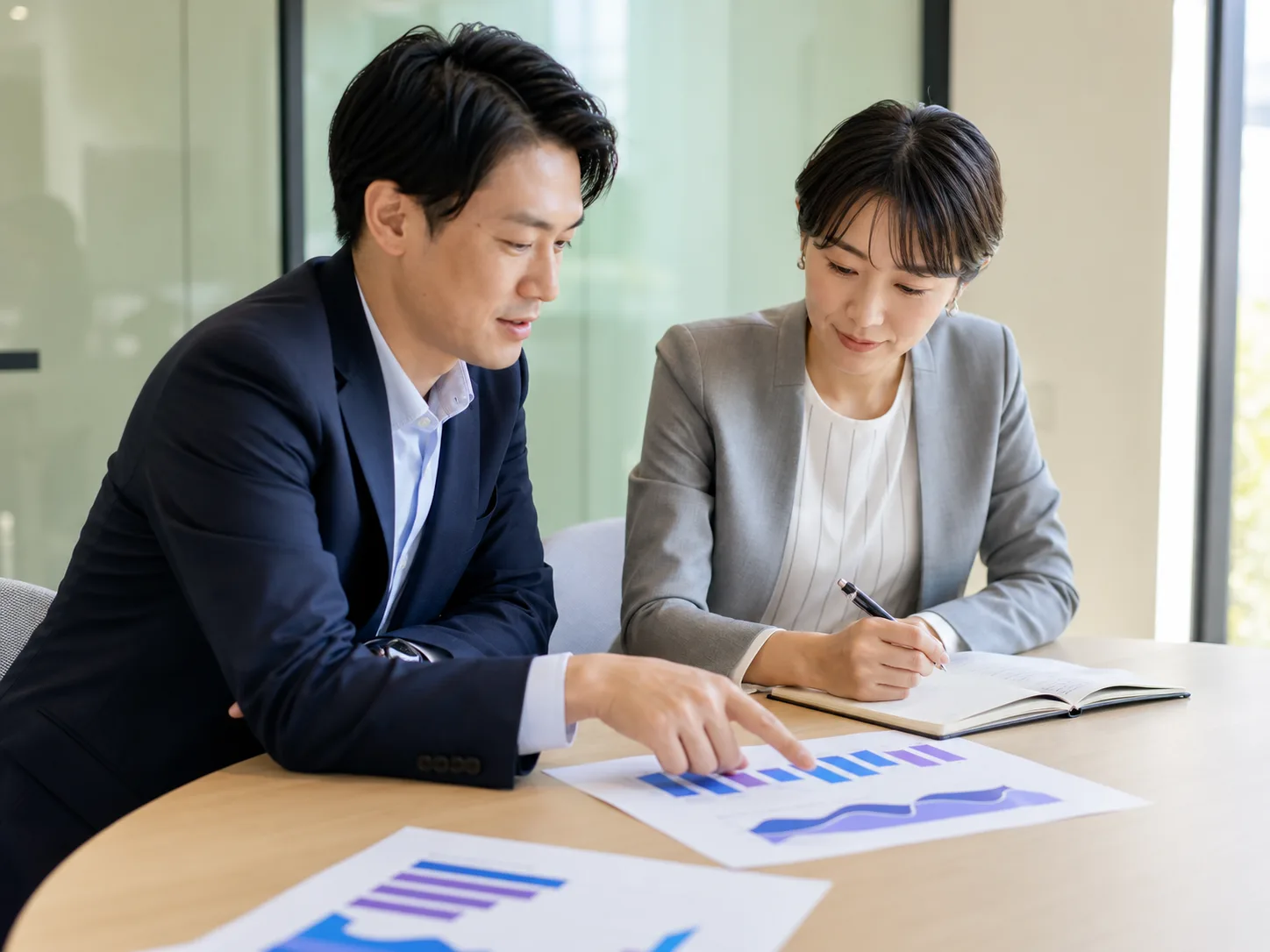 資料のグラフを指しながら、次の打ち手を打ち合わせしている2人のビジネスパーソン